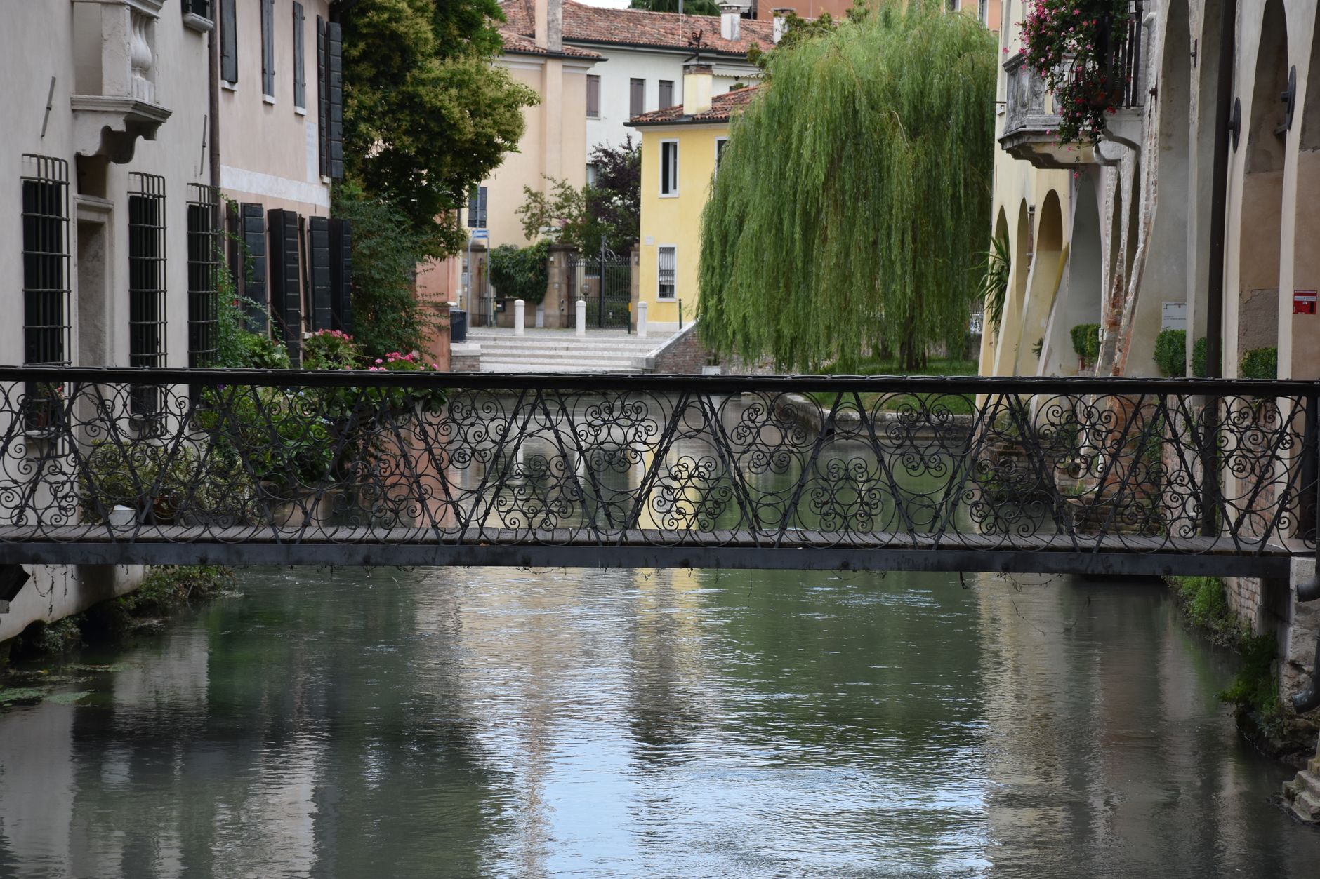 A picturesque view of a wrought iron bridge over a canal in historic Treviso, Italy.