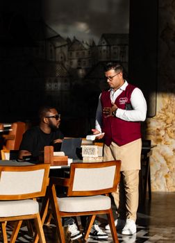 A waiter in uniform serves a customer in a trendy Dubai cafe with unique decor.
