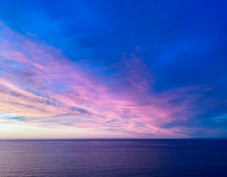 Vibrant sunset over the ocean with stunning pink and blue clouds.
