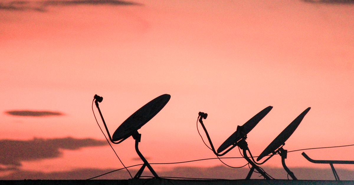 Photo by Saravanan Narayanan A row of satellite dishes silhouetted against a vibrant orange sunset sky on a rooftop.