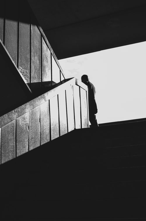 Free Dramatic black and white photo of a silhouetted figure on a staircase, capturing contrast and mood. Stock Photo