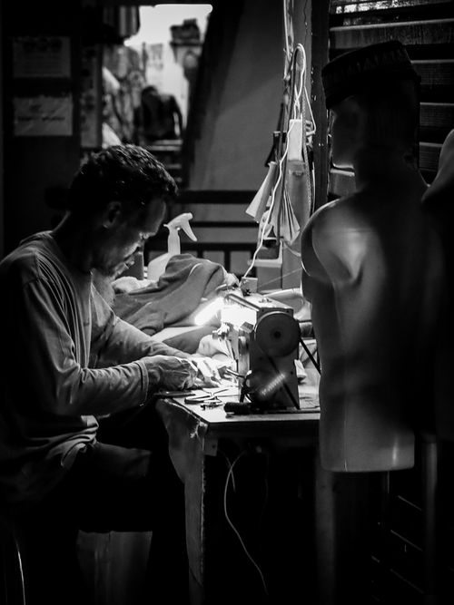 Free A focused tailor works with a sewing machine in a dimly lit workshop, captured in black and white. Stock Photo
