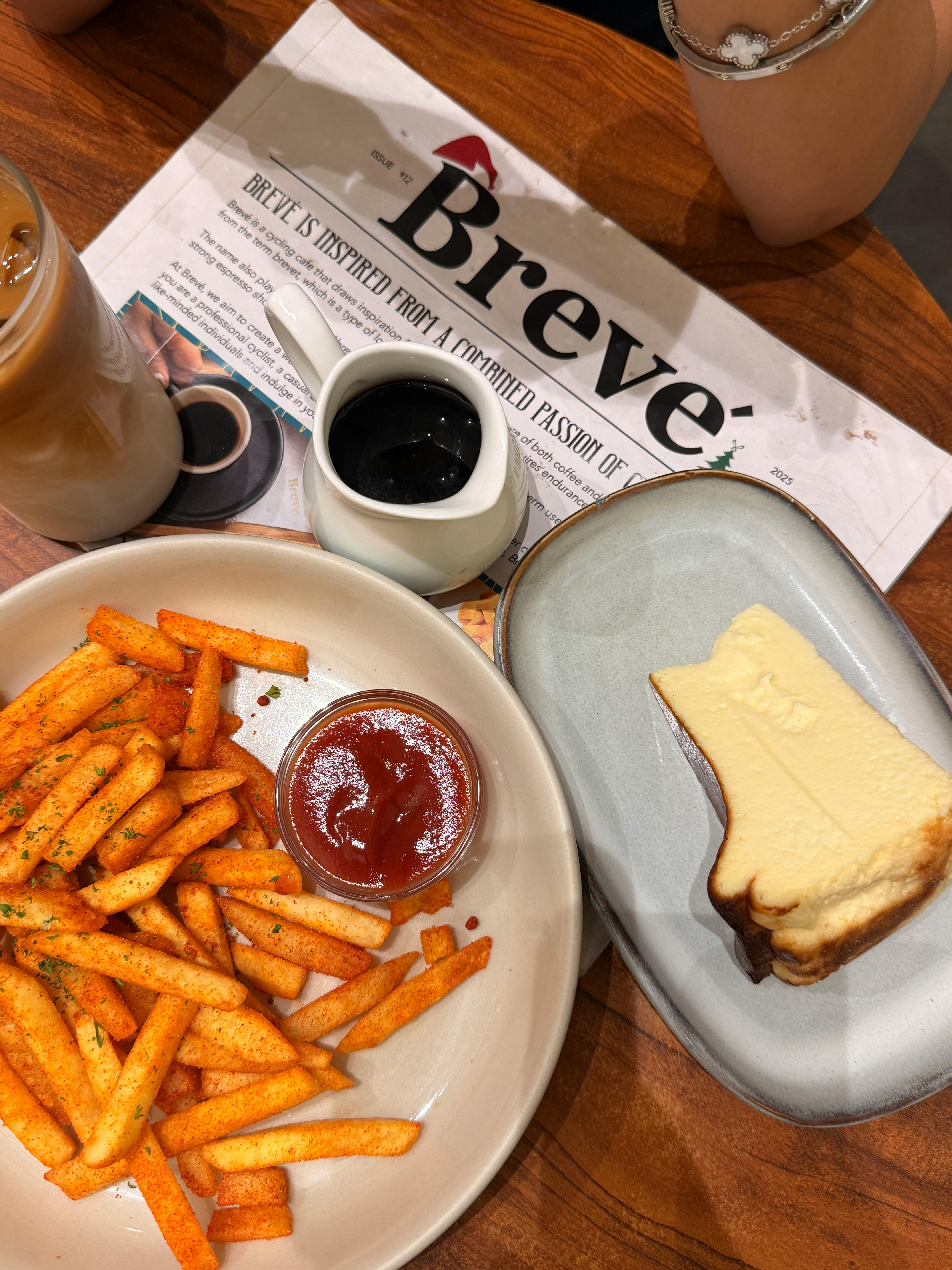 Overhead view of spiced fries, cheesecake, and iced coffee at a cafe table setting.