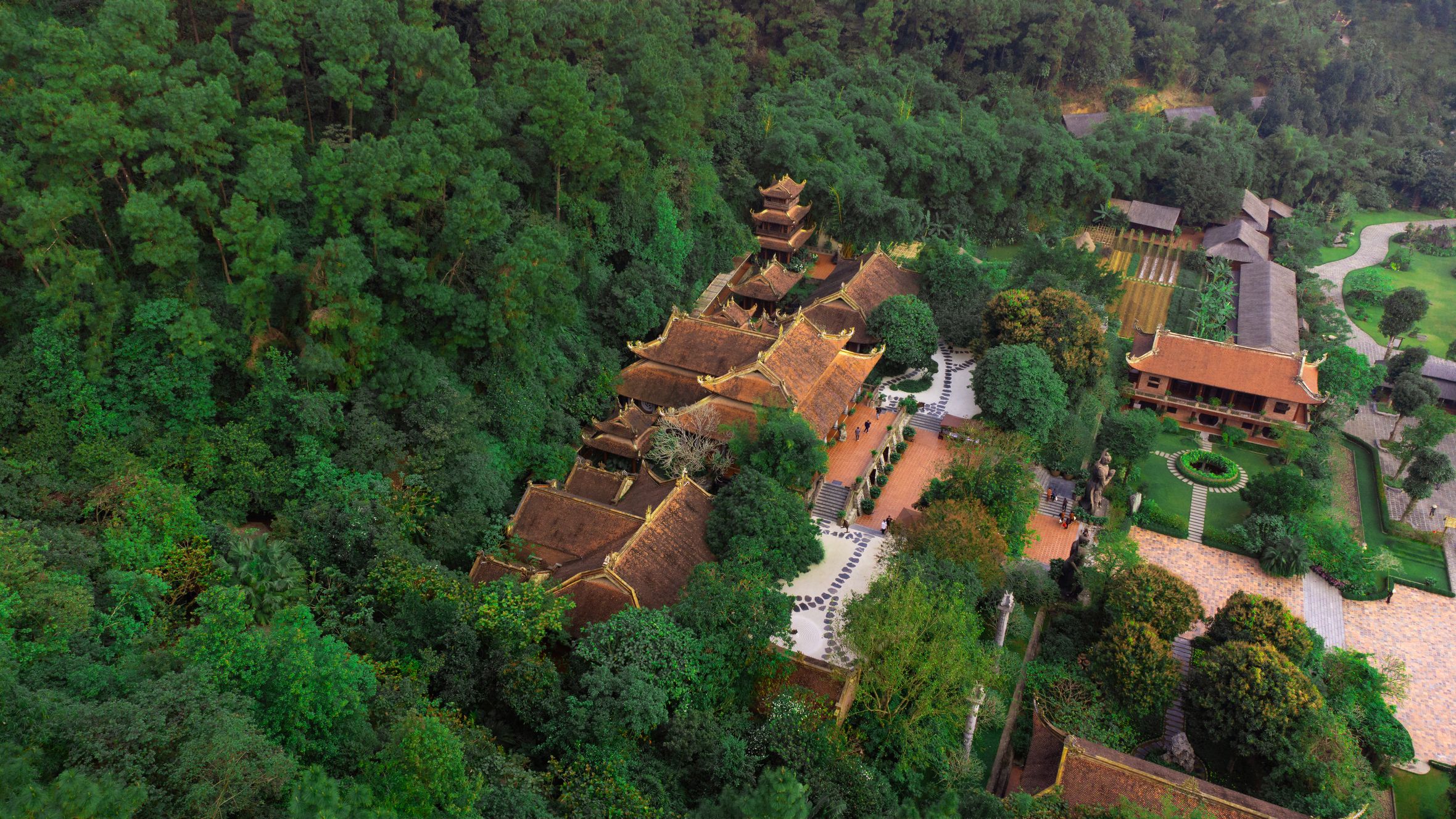 Aerial view of a traditional Vietnamese temple surrounded by lush greenery, capturing the serene atmosphere and architectural harmony.