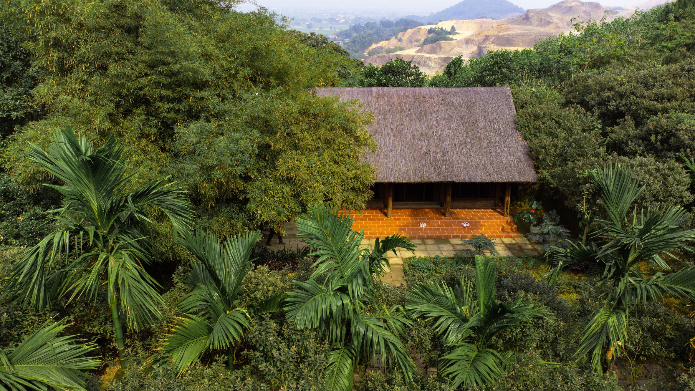 Aerial photo of a traditional hut surrounded by lush tropical vegetation and greenery in a forest landscape.