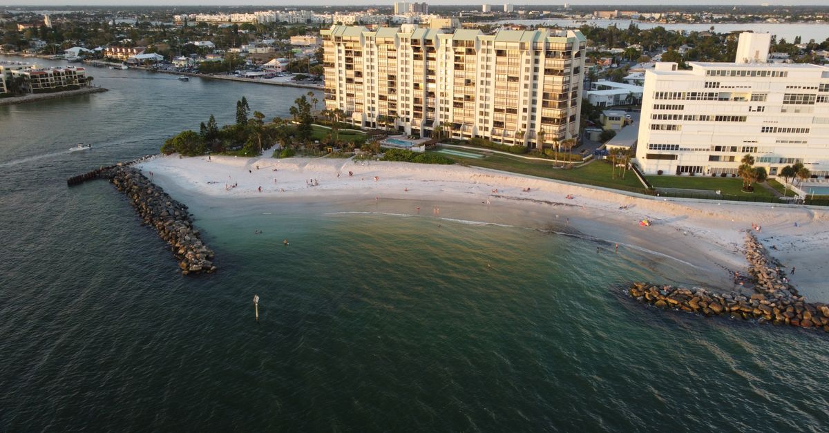 Aerial shot of a serene beach with high-rise apartments and calm waters during sunset.