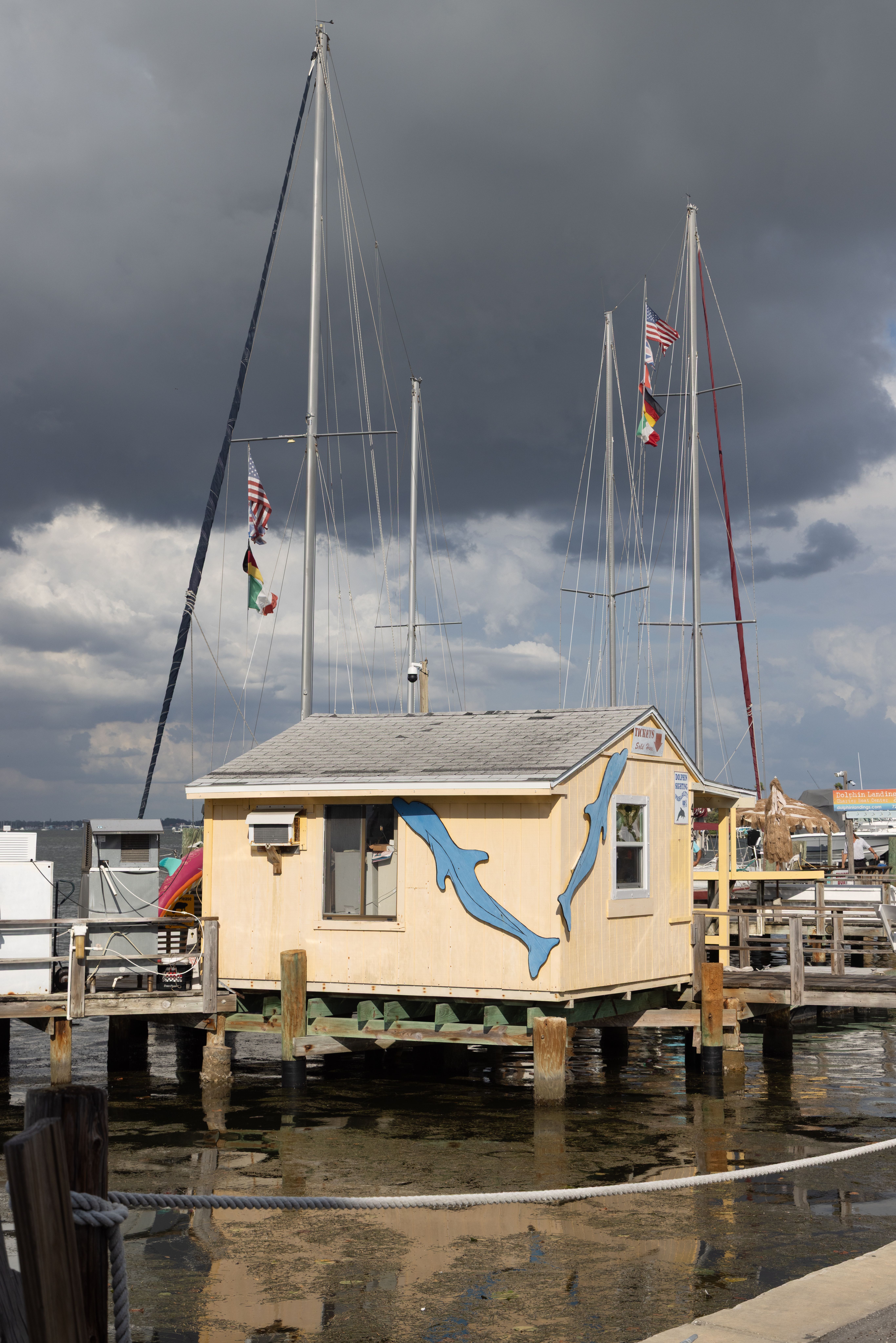 A small cabin sits over the water with a dolphin mural under a dramatic, stormy sky.