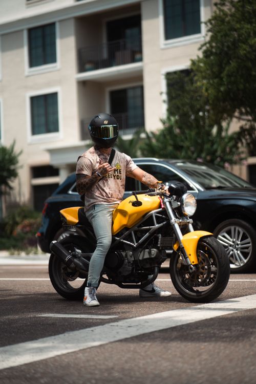 Free A biker on a yellow motorcycle stops at a city intersection, wearing helmet and casual attire. Stock Photo