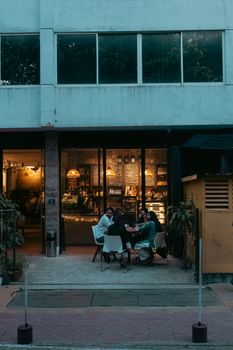 A group of adults enjoy an evening at an outdoor cafe table, warmly lit from inside.