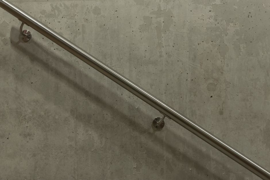A minimalist image of a stainless steel handrail mounted on a concrete wall.