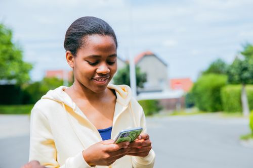 Free A smiling young woman uses her smartphone in a sunny outdoor setting in Brussels, Belgium. Stock Photo