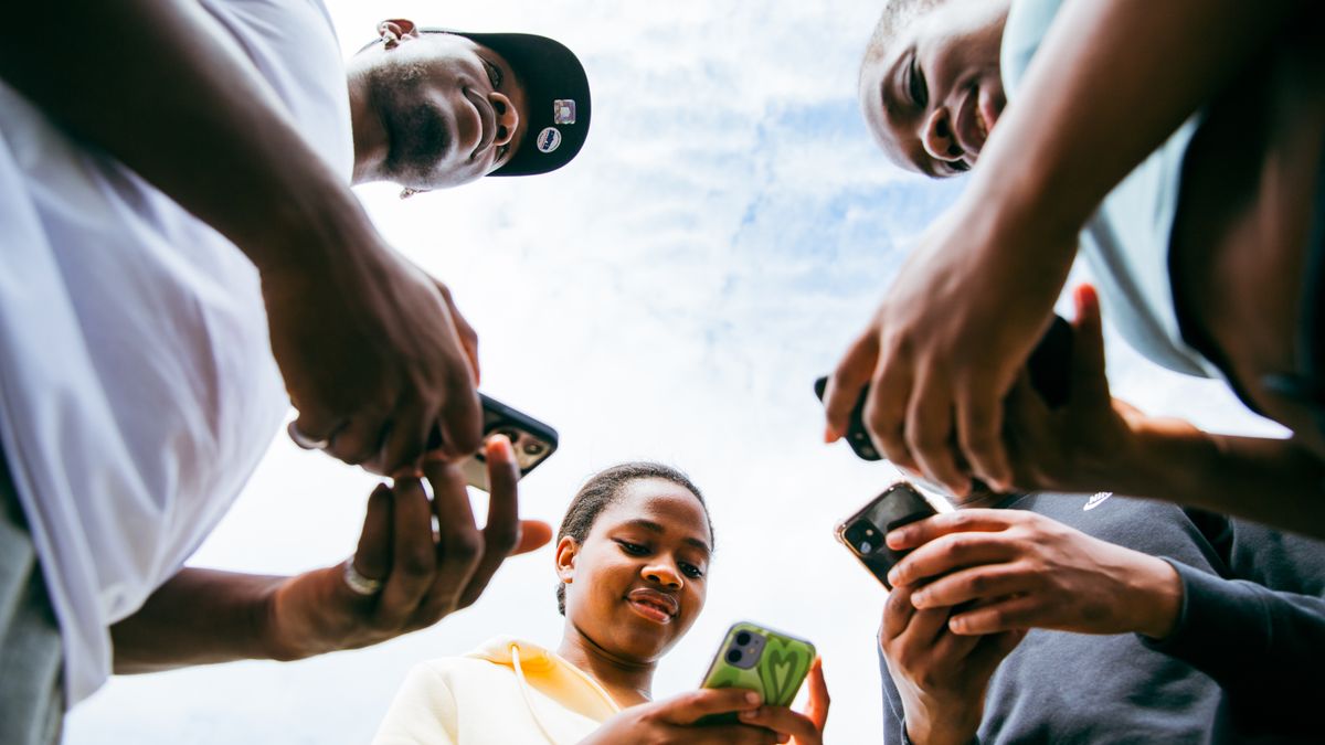 Friends standing in a circle, each looking at their own phone, seen from below