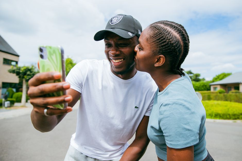 Smiling couple taking a selfie with smartphone in Brussels. Capturing joyful moments outdoors on a sunny day.