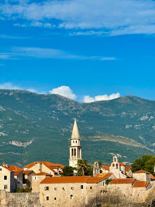 Free Beautiful view of Montenegro's old town with a tower and mountains in the background under a clear blue sky. Stock Photo