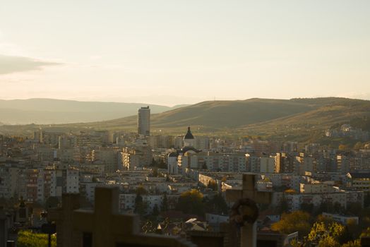 A scenic view of Cluj-Napoca city against the backdrop of rolling hills at sunset.