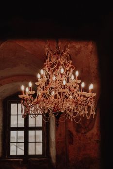 A vintage chandelier with crystal adornments glows warmly in a dimly lit room, evoking classic elegance.