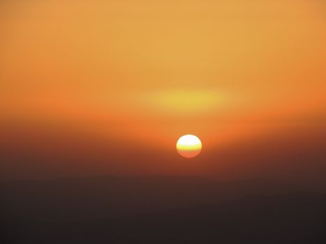 Vibrant orange sunset with the sun setting over silhouetted hills. Perfect for tranquil and scenic themes.