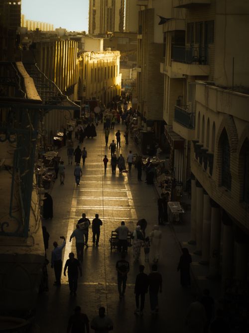 Free Silhouetted pedestrians walk along a bustling urban street with historic architecture at dusk. Stock Photo