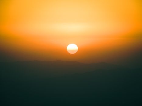 A tranquil sunrise over misty mountains with a vibrant orange sky.