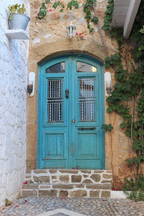 Free A vibrant blue door set in rustic Greek stonework, adorned with ivy. Stock Photo