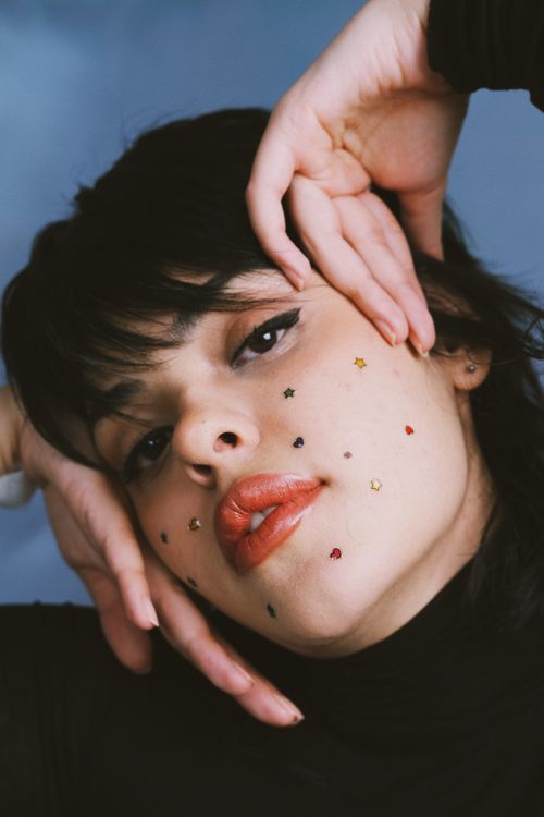 Free Close-up portrait of a woman with colorful star stickers and bold makeup in a thoughtful pose. Stock Photo