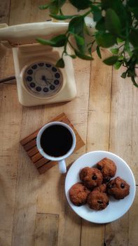 Cozy scene of black coffee with chocolate chip cookies and a vintage rotary phone on a wooden table.