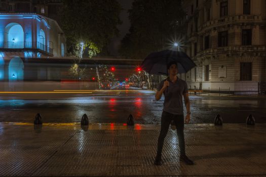 Man holding an umbrella on a rainy night in the city, with bright lights and blurred motion.