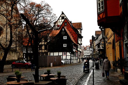 Historic half-timbered houses on a cobblestone street in Quedlinburg, Germany, with people strolling by.