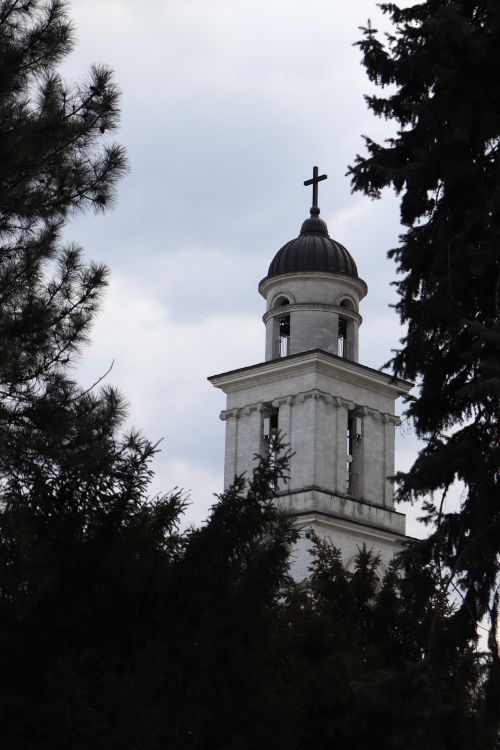 Free A beautiful church tower emerges through dense trees under a cloudy sky in Chișinău, Moldova. Stock Photo