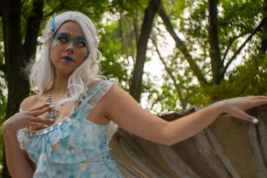 A mystical fairy woman in costume poses elegantly in a lush, green forest backdrop.