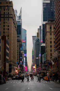 Urban scene in Times Square, New York City at dusk with people crossing street.