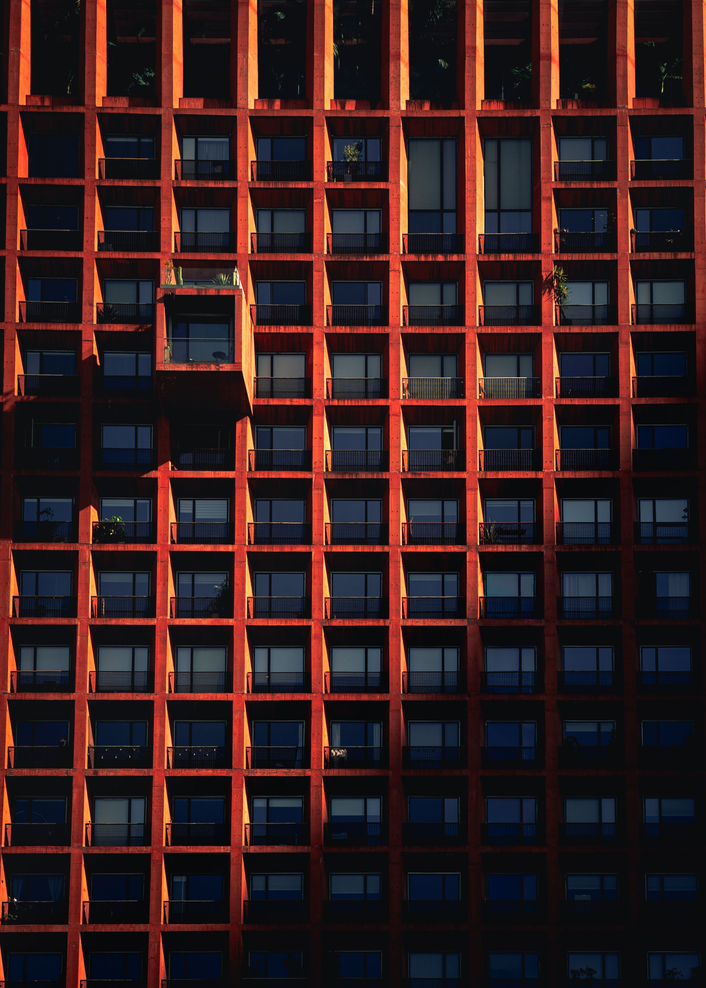 A striking geometric facade with red grid structure under bright sunlight.