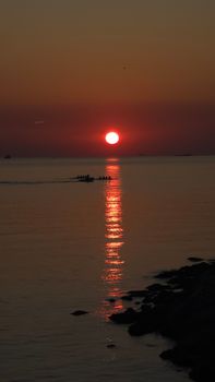 A breathtaking silhouette of rowers at sunset with the sun reflecting on the calm sea surface.