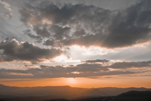 A breathtaking sunset with golden hues casting over a mountainous landscape and dramatic clouds.