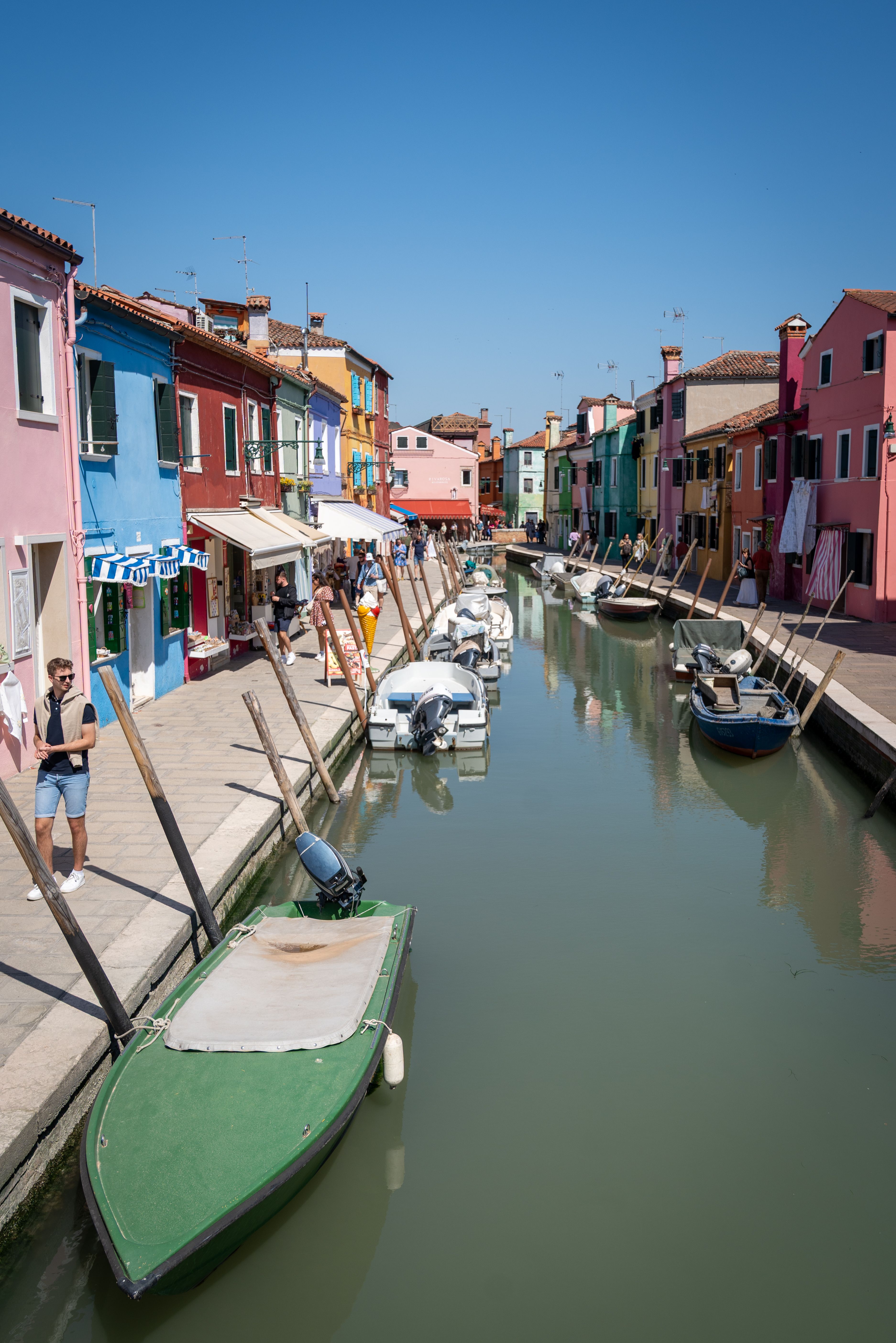 Vibrant Burano canal with colorful houses and boats on a sunny day in Italy.