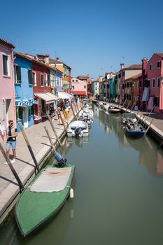 Vibrant Burano canal with colorful houses and boats on a sunny day in Italy.