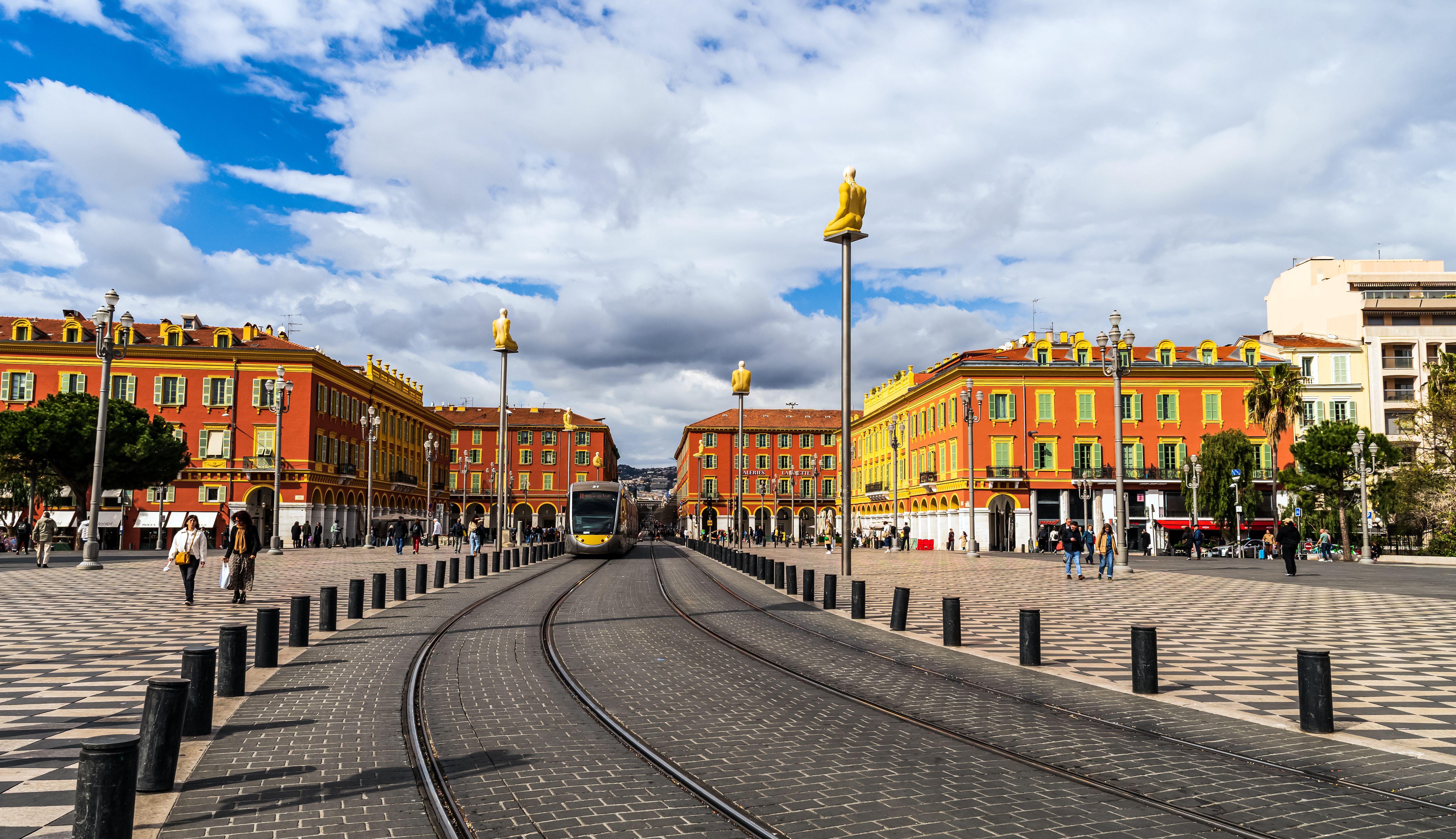 Tram passing through the colorful Place Masséna in Nice, France, under a blue sky.