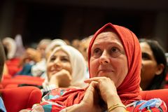 Diverse audience members attentively watching a speaker at a cultural event indoors.