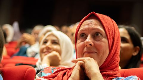 Diverse audience members attentively watching a speaker at a cultural event indoors.
