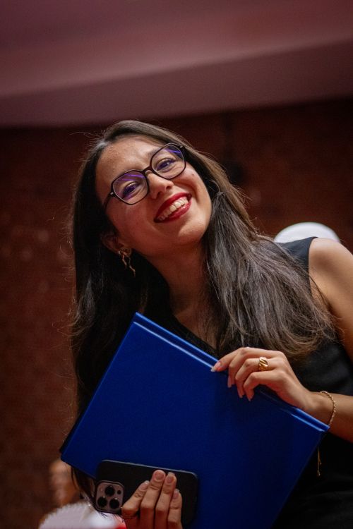 Free Portrait of a joyful woman wearing glasses, holding a blue folder indoors. Stock Photo
