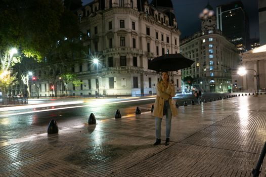 A woman stands holding an umbrella at night in Buenos Aires, capturing city lights and architectural charm.