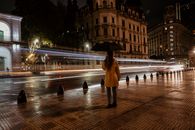 A lone figure with an umbrella stands in a rainy Buenos Aires street, Argentina at night.