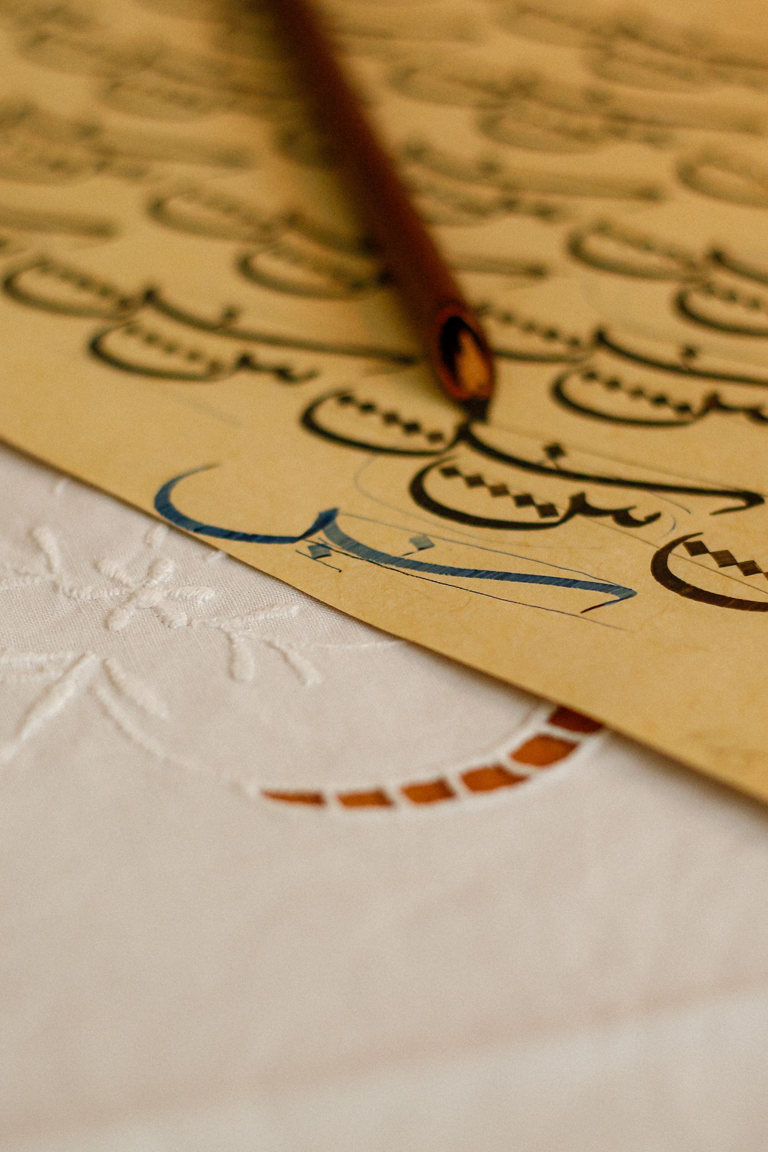 Close-up of Arabic calligraphy practice with a pen on textured paper.