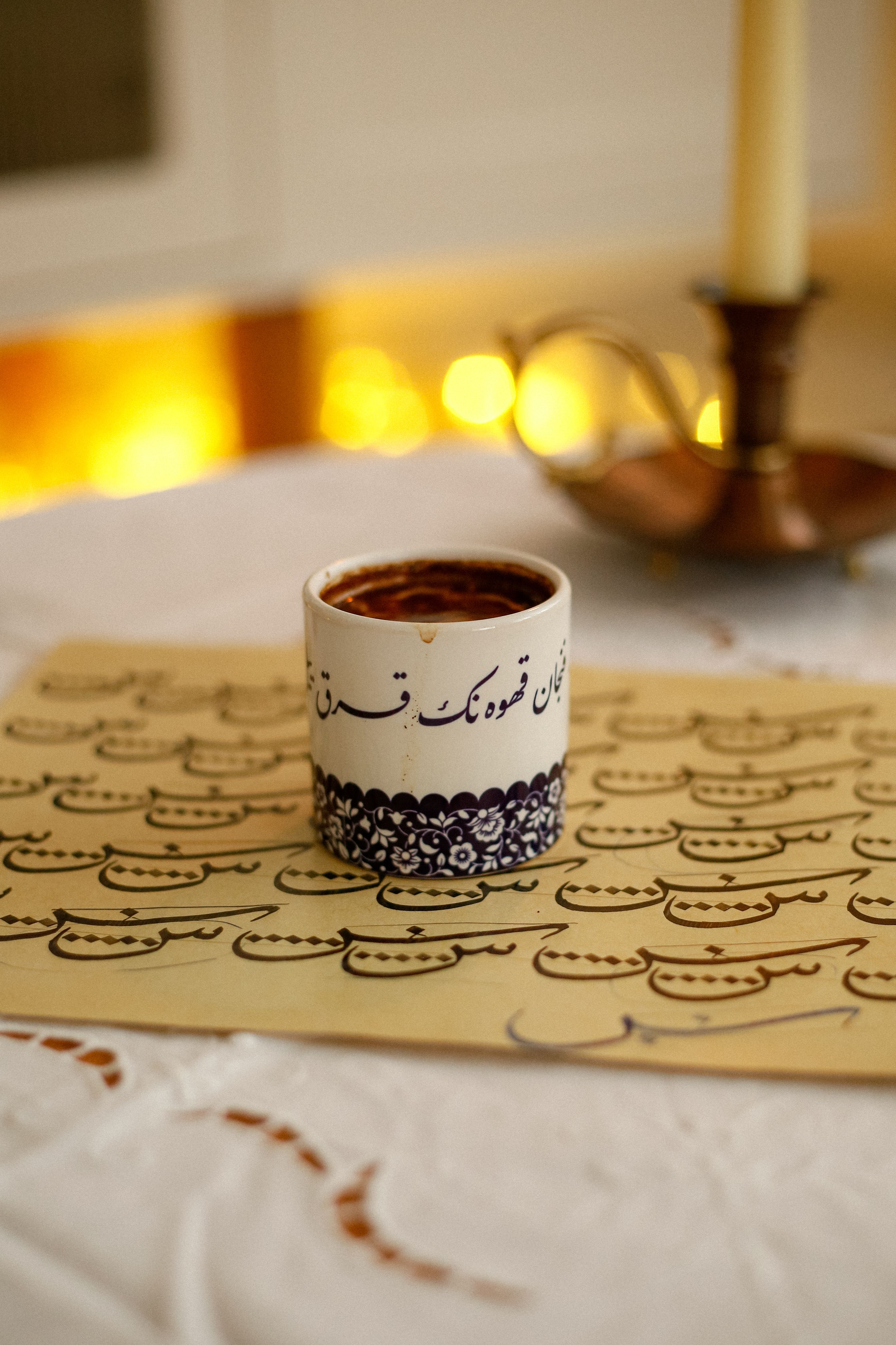 A coffee cup with Arabic calligraphy, set against a backdrop of elegant decor and candlelight ambiance.