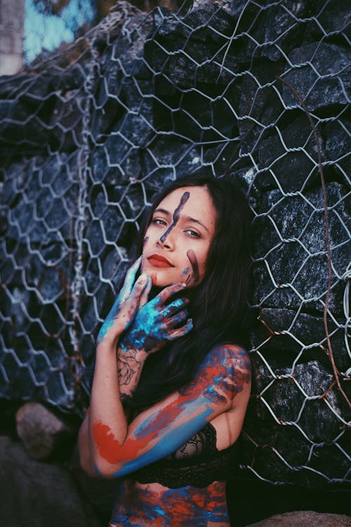 Painted Skin Woman Leaning on Black  Rock Wall