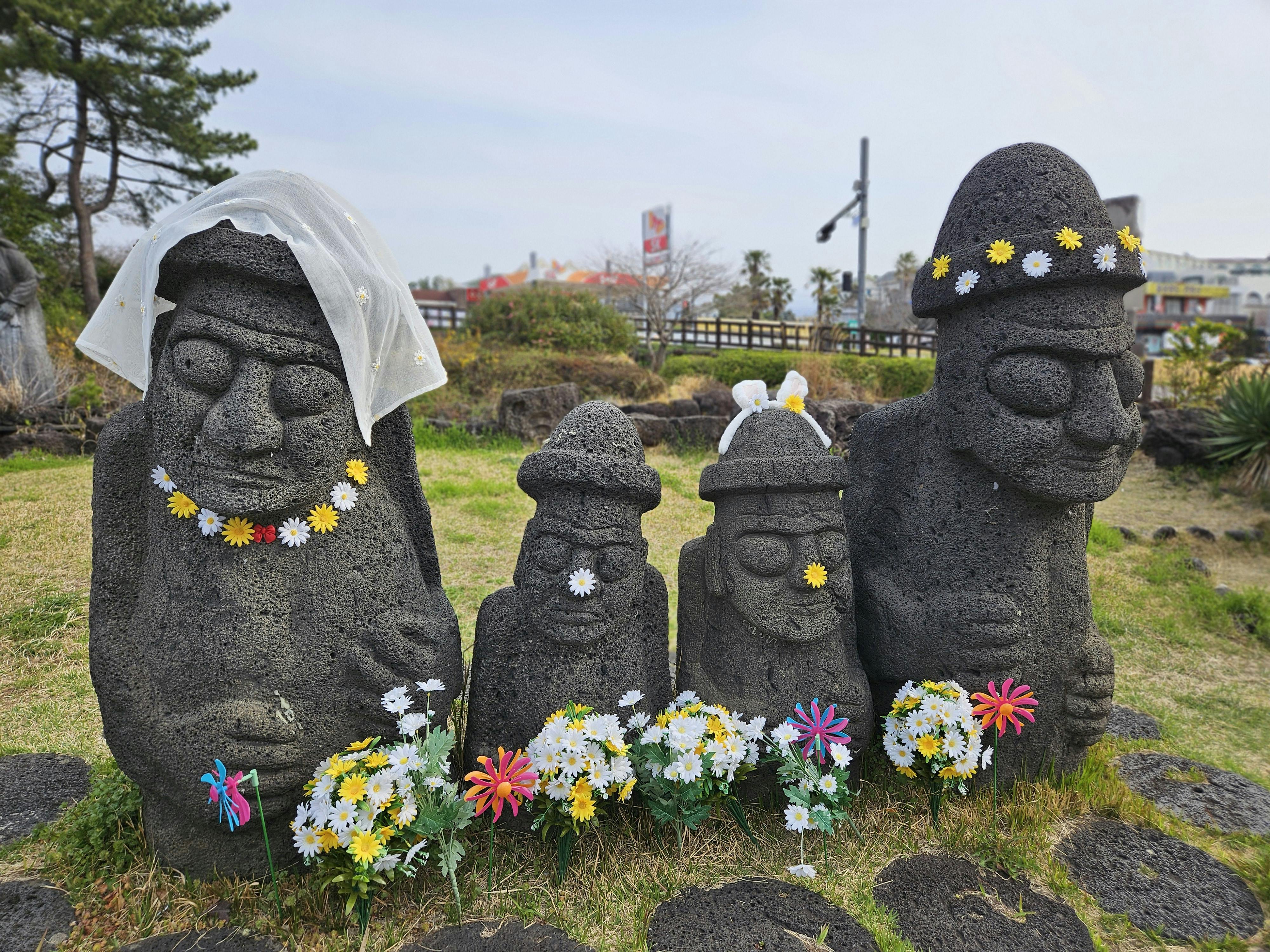 Dol Hareubang statues adorned with flowers and veils on Jeju Island, South Korea.