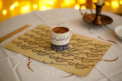 Free Elegant coffee cup on Arabic calligraphy with warm bokeh lighting, perfect for cultural and artistic themes. Stock Photo