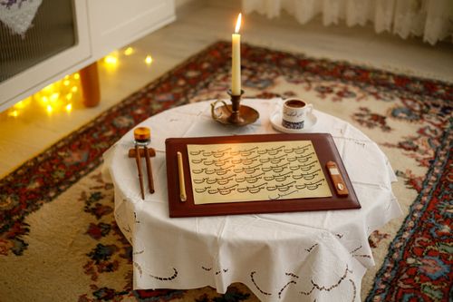 Free Warm indoor scene featuring calligraphy, a lit candle, and a cup of tea on a small table. Stock Photo