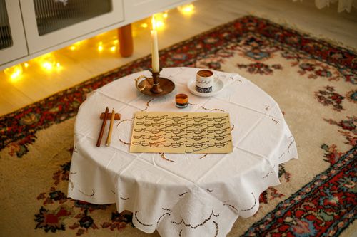 Free An intimate indoor setting featuring a table with candles, coffee, and calligraphy tools on a patterned rug. Stock Photo