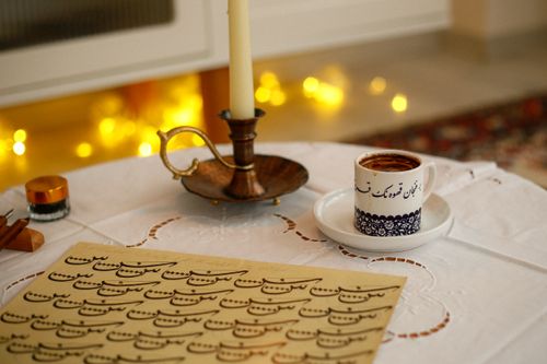 Free A decorative calligraphy set with a candle and coffee cup on a table, creating a warm ambiance. Stock Photo